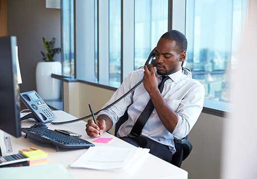 man sitting behind his desk talking on a landline
