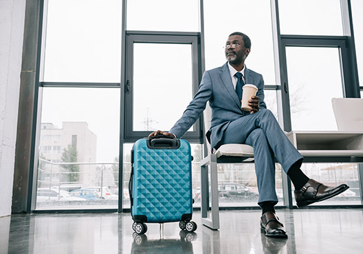 man sitting in foyer with his hand on his luggage and a cup in his hand